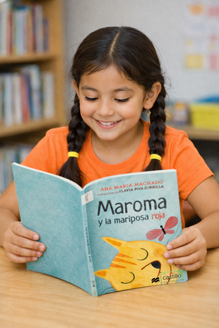 A young girl with braids happily reading a book titled 'Maroma y la mariposa roja' in a library setting.