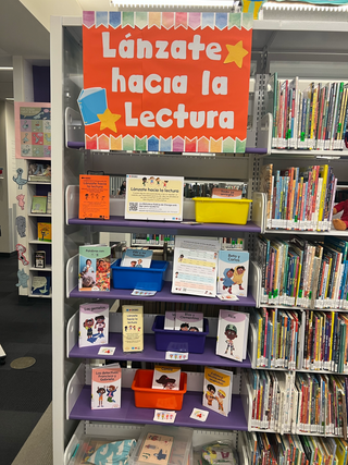 Library bookshelf with colorful signage and children's books supporting the program for Lánzate hacia la lectura.