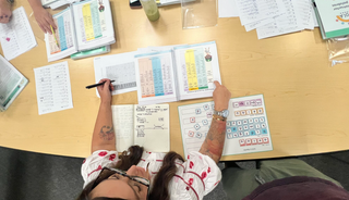 Person filling out forms at a desk with various documents and a pen.